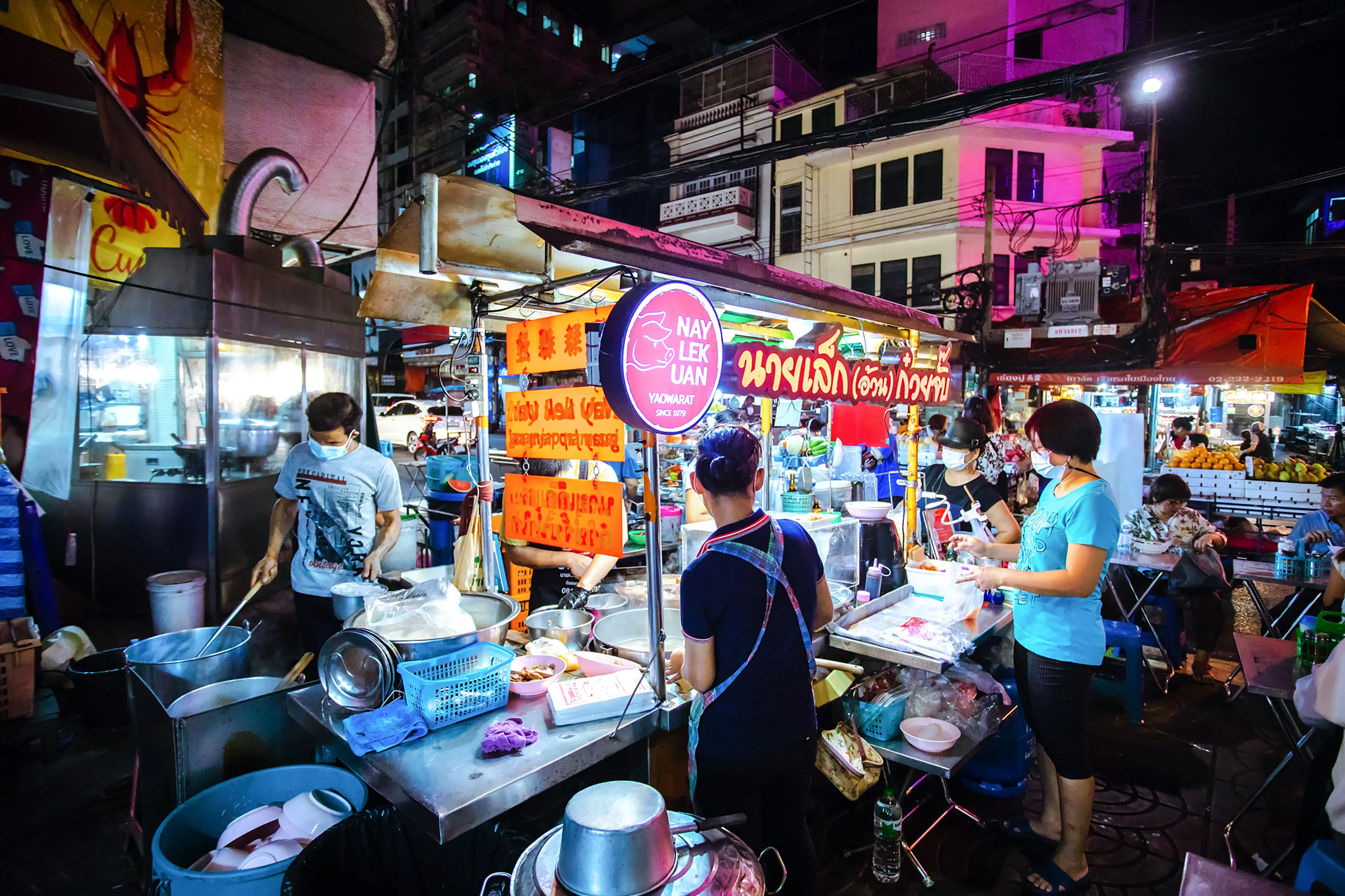Three people are preparing  selling rolled noodle soup with crispy pork at a street food stall in Bangkok