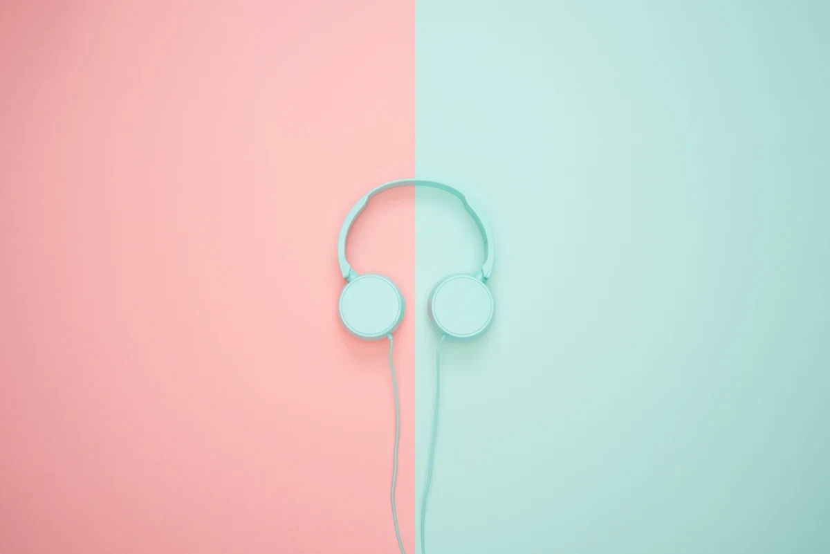 Mint green over-the-ear headphones rest against a color-blocked background. The left half of the background is the same mint green as the headphones. The right half is a rosy pink.