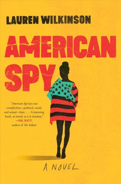 Hardcover of 'American Spy.' It features a black silhoutted figure draped in an American flag in which the blue field was replaced by green, and the white stripes were replaced by black ones, to reflect the colors of the Pan-African flag (red, black, and green). The author's name, Lauren Wilkinson, is in red text. The title is black text. It's all set against a deep yellow background.