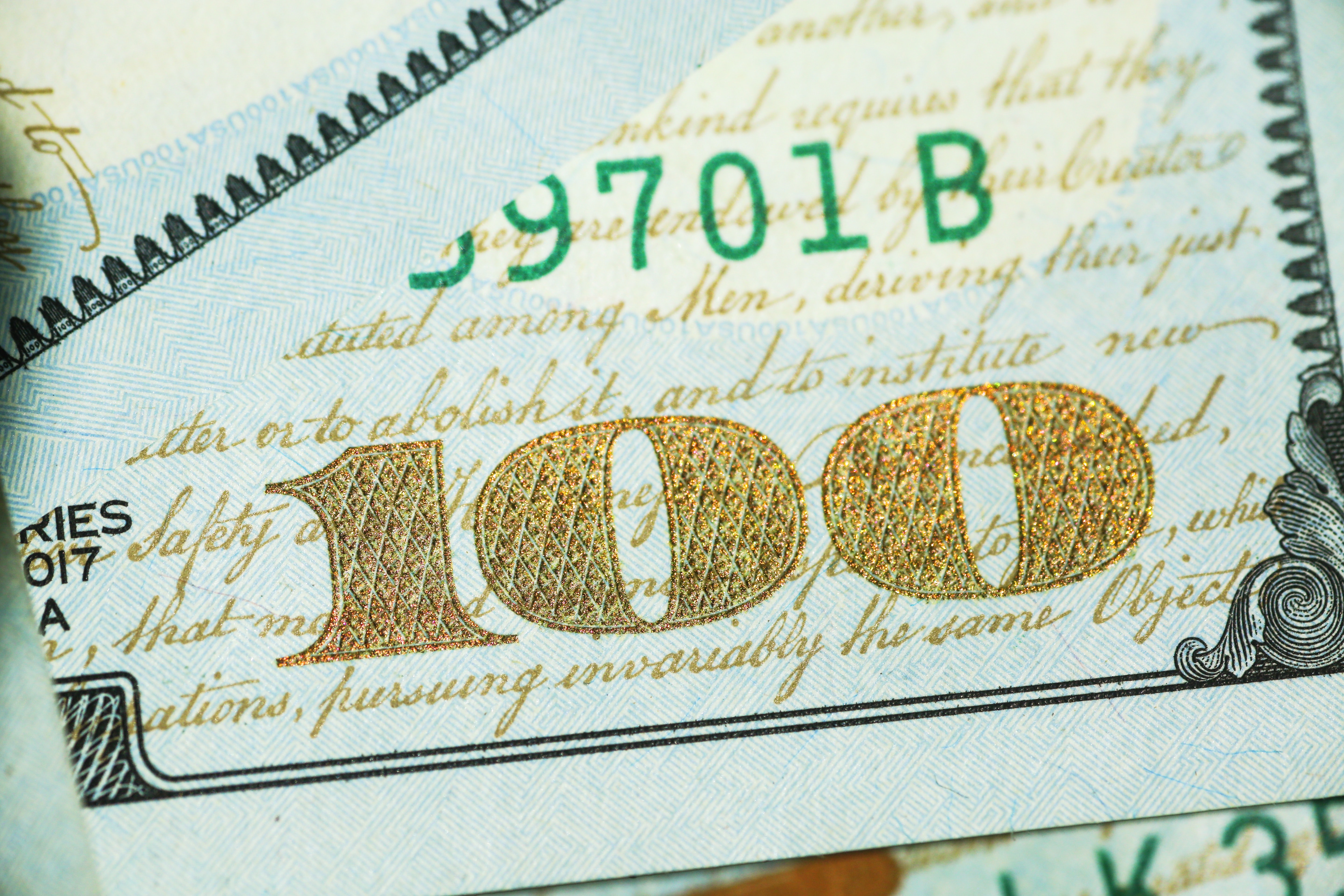 A shimmering golden number one hundred in the corner of a United States one hundred dollar bill.