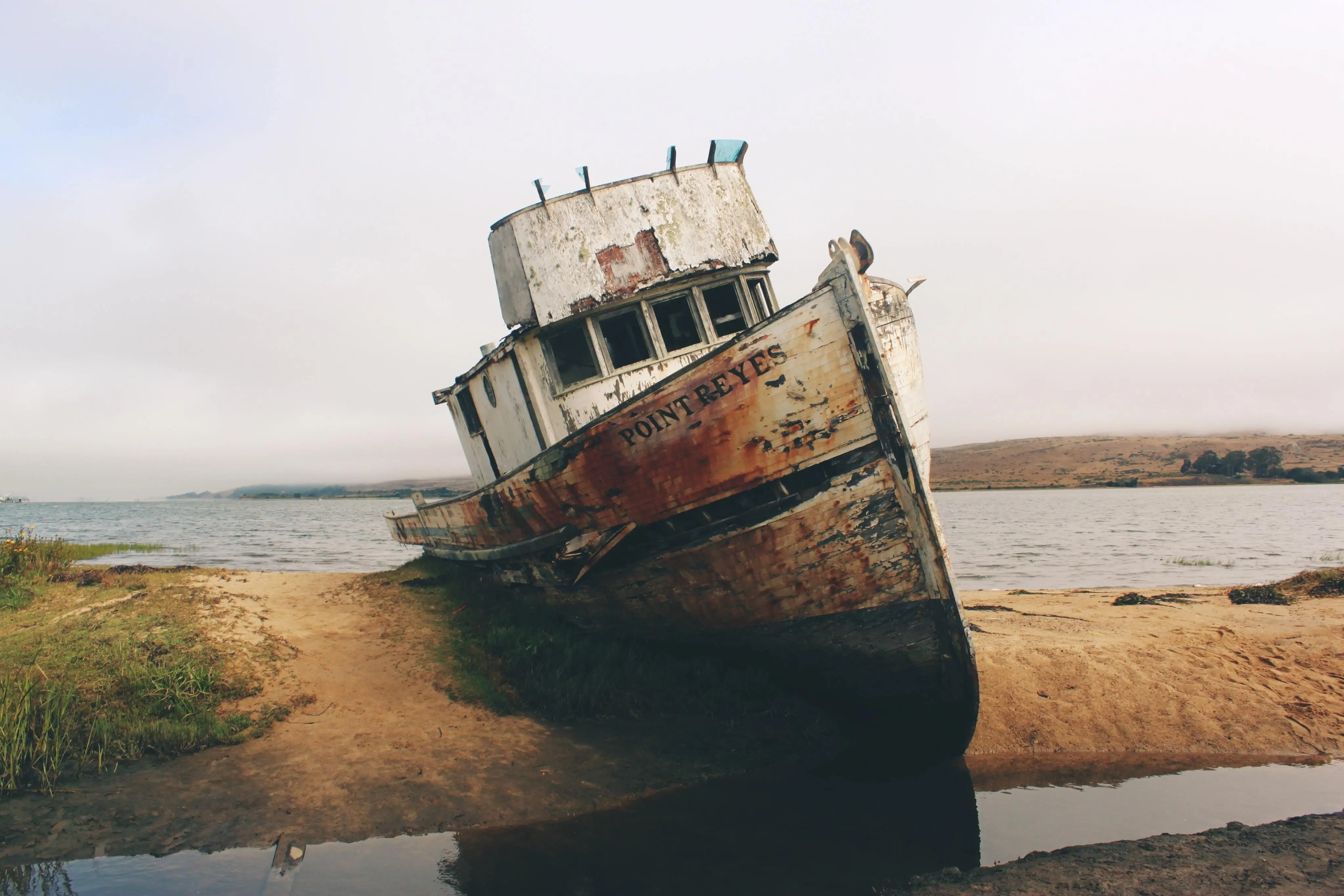 An old rusting tug boat that’s run aground. Its white paint is peeling. ’Point Reyes’  is painted across its bow.