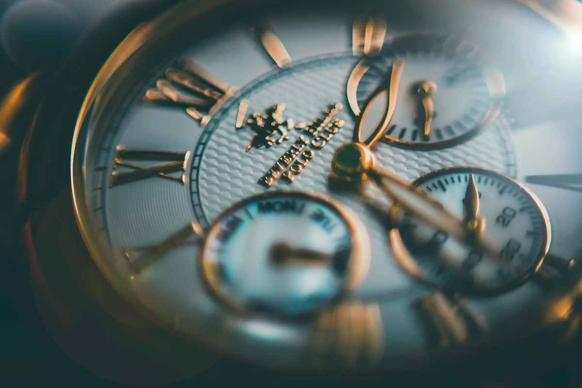 A macro lens perspective of a watch face from the Beverly Hills Polo Club brand. The watch has with gold tone numerals against a textured white dial. The watch also has three subdials that track the day of the week, minute, and seconds.