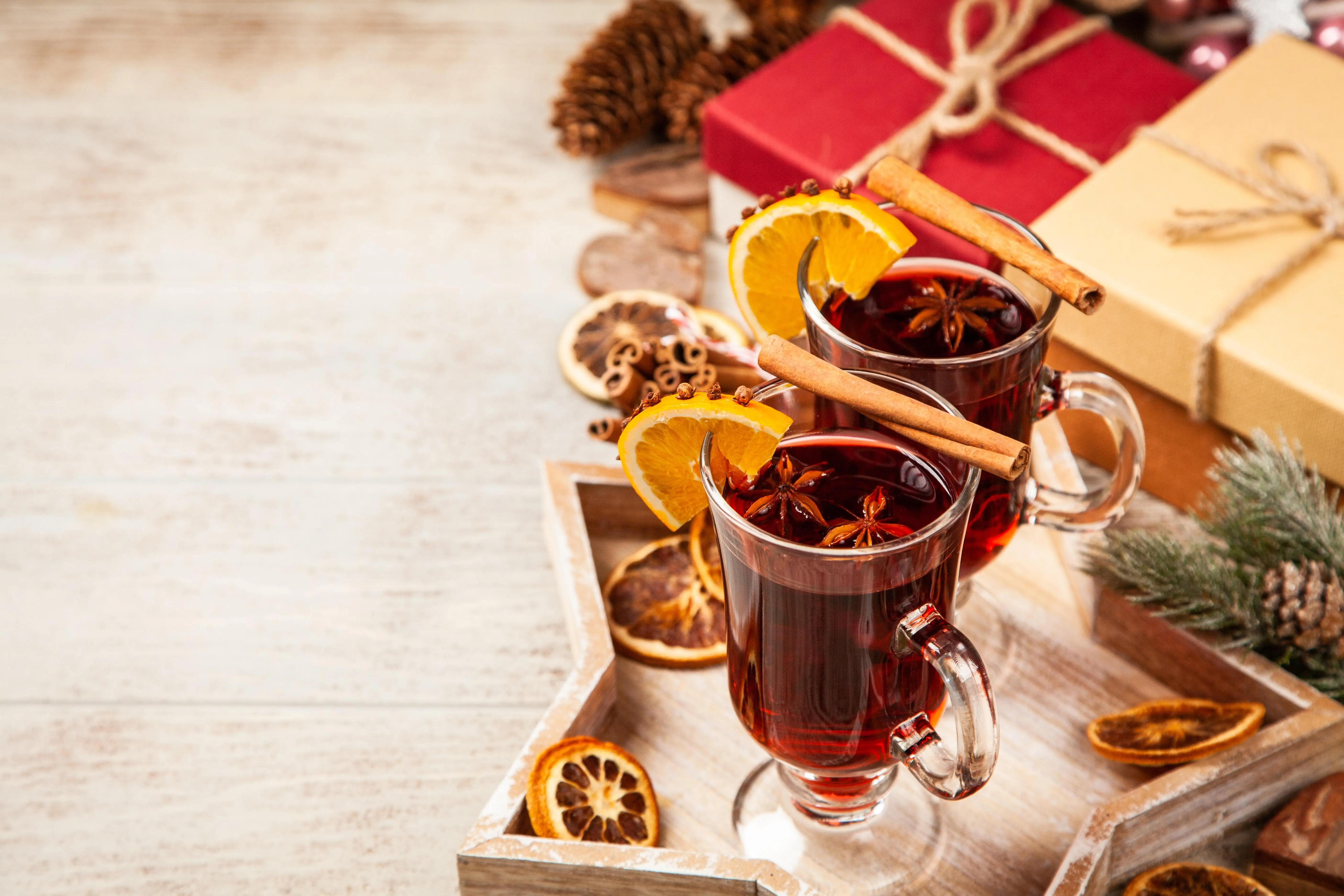 Two clear footed glass mugs on a wooden star-shaped tray. Both mugs are filled with mulled wine that's garnished with a clove-studed orange slice, star anise pods, and a cinnamon stick.