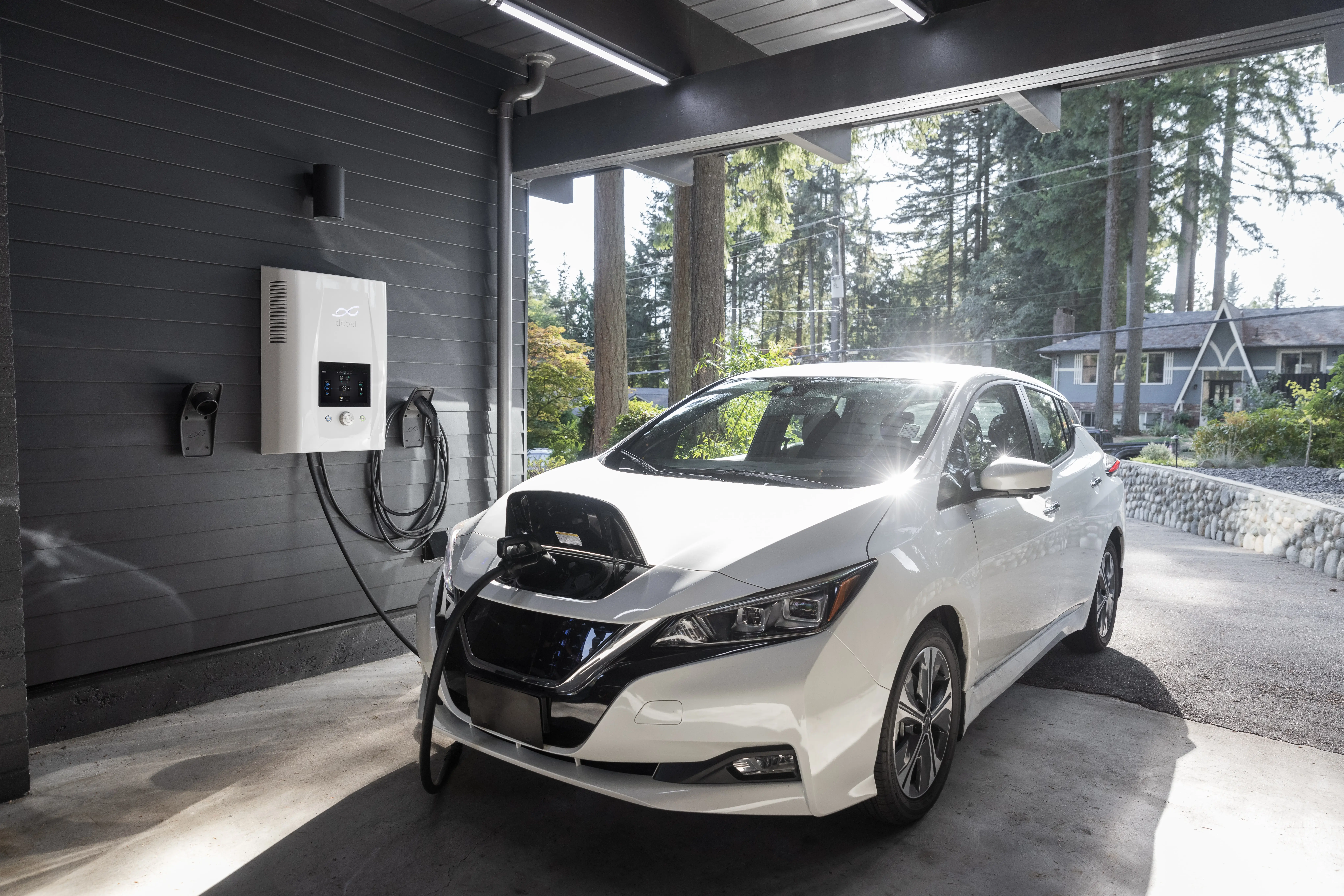 A white electric-powered Nissan Leaf car charges in a garage.