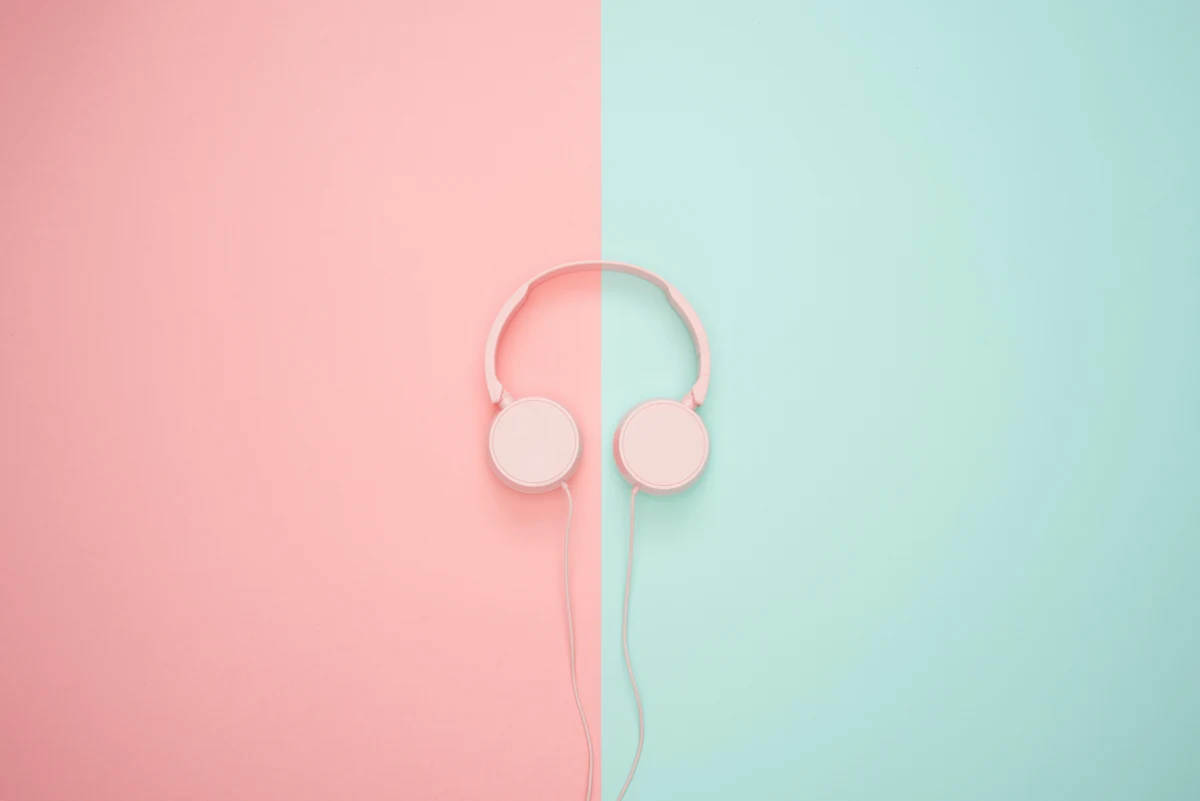 Rose pink over-the-ear headphones rest against a color-blocked background. The left half of the background is the same rosy pink as the headphones. The right half is mint green.