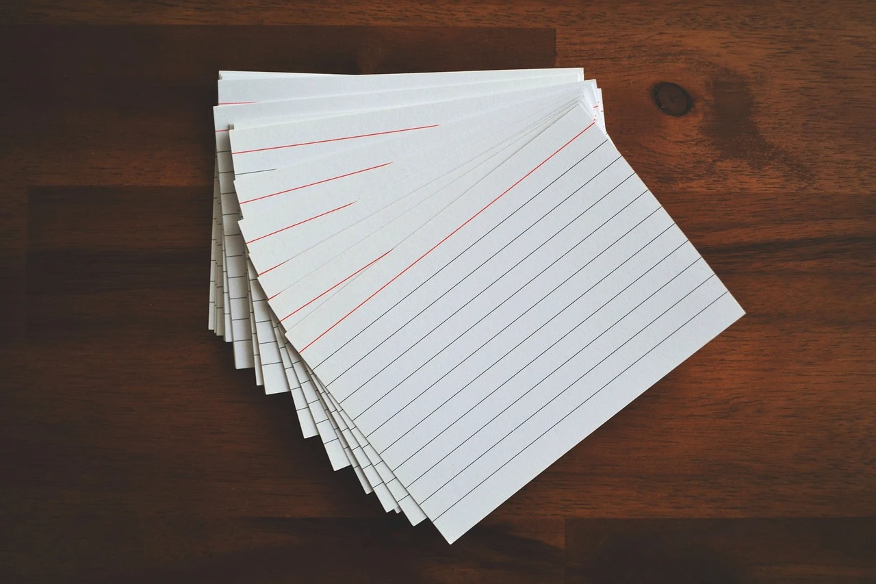 A thick stack of blank index cards on a dark wood table top. The cards are slightly fanned.