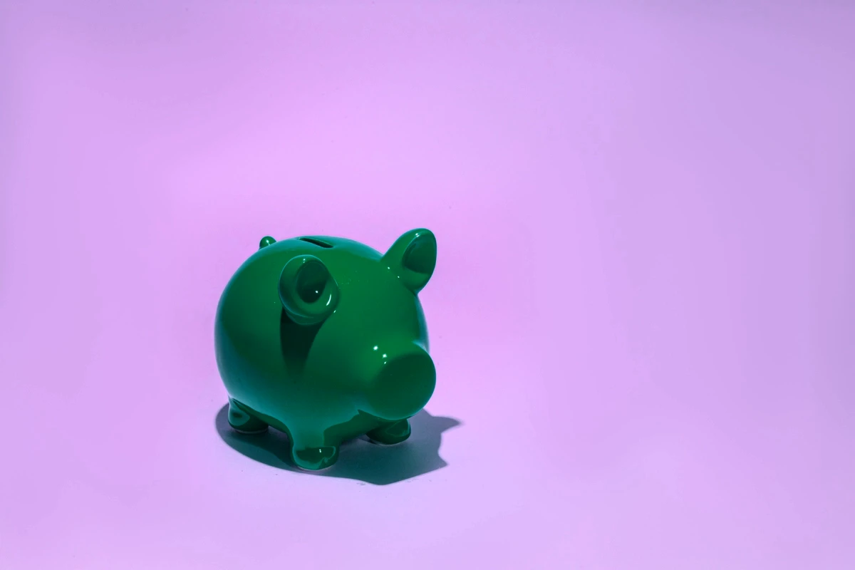 A small forest green, ceramic pig-shaped bank set against a lavender-colored background.