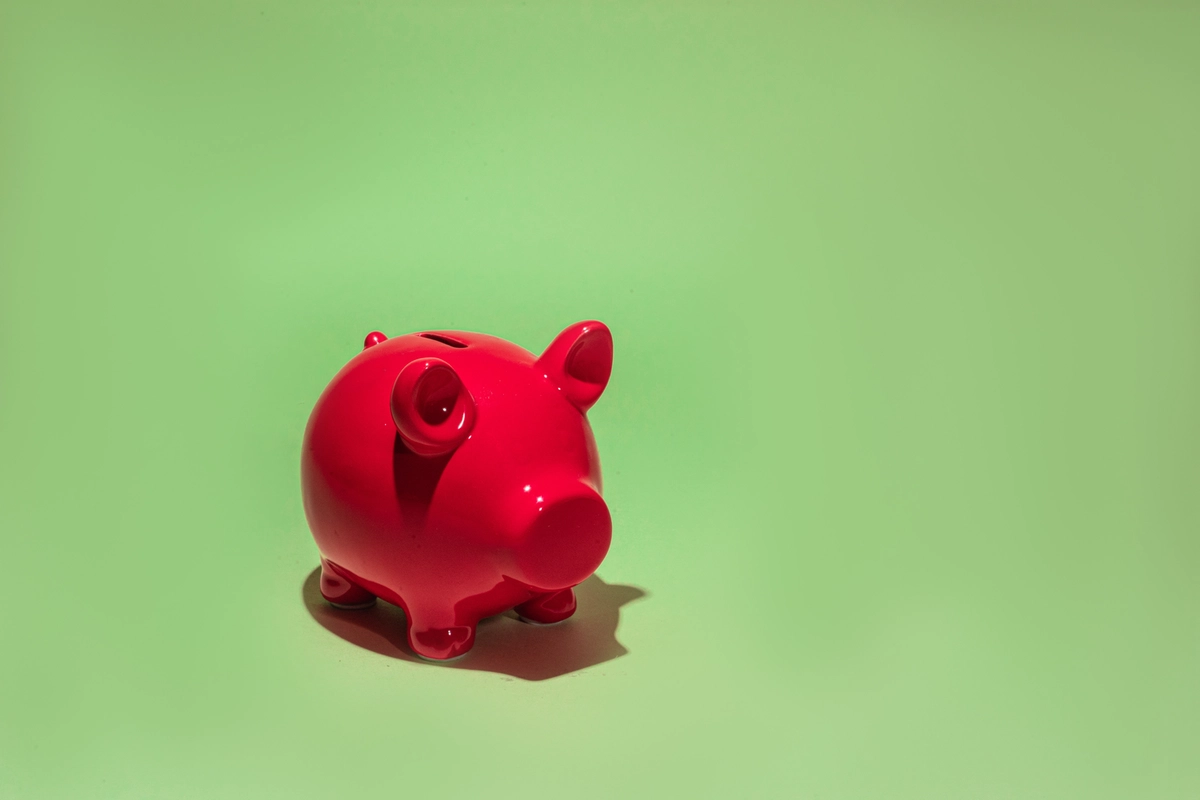 A small red, ceramic pig-shaped bank set against light-green colored background.